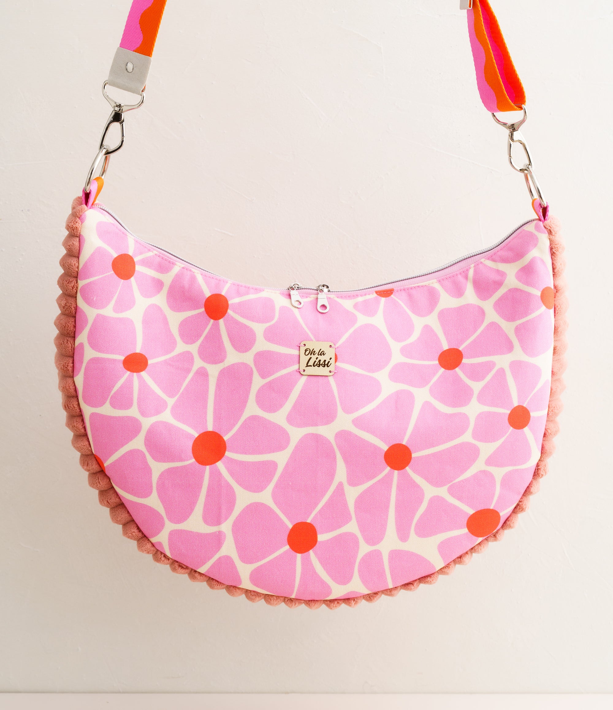 Handgemachte Schultertasche für Damen aus Baumwollstoff mit rosa Blumenmuster und orangefarbenen Details, halbmondförmige Tasche mit Reißverschluss und breitem Gurt.