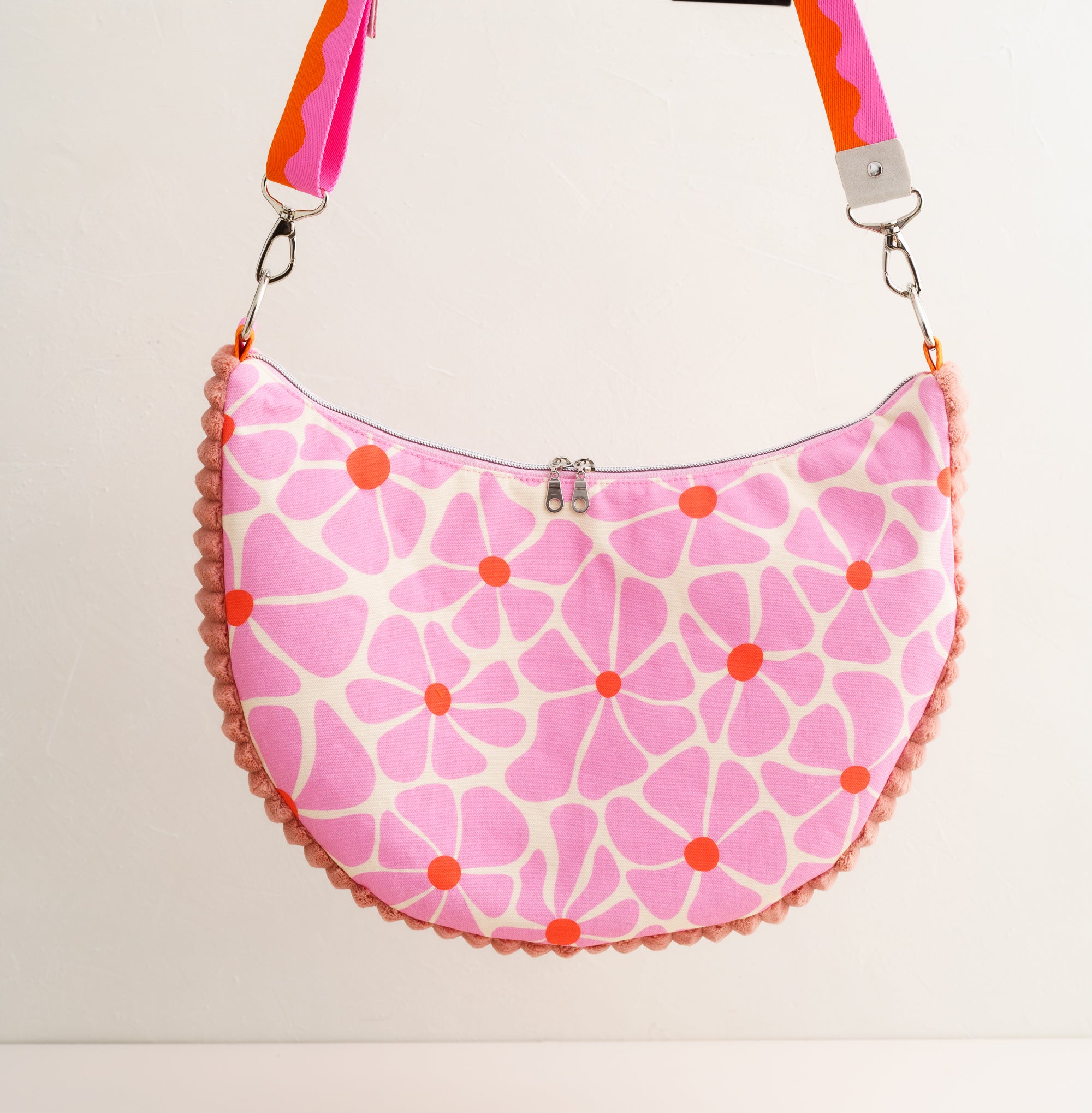 Handgemachte Schultertasche für Damen aus Baumwollstoff mit rosa Blumenmuster und orangefarbenen Details, halbmondförmige Tasche mit Reißverschluss und breitem Gurt.
