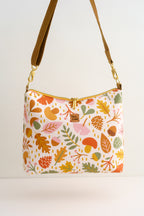 Eine Umhängetasche mit einem farbenfrohen Herbstmuster aus Blättern, Eicheln und Pilzen. Die Tasche hat einen braunen Riemen, goldfarbene Beschläge und einen goldenen Reißverschluss. Der Text "Oh la Lissi" befindet sich auf der Tasche.